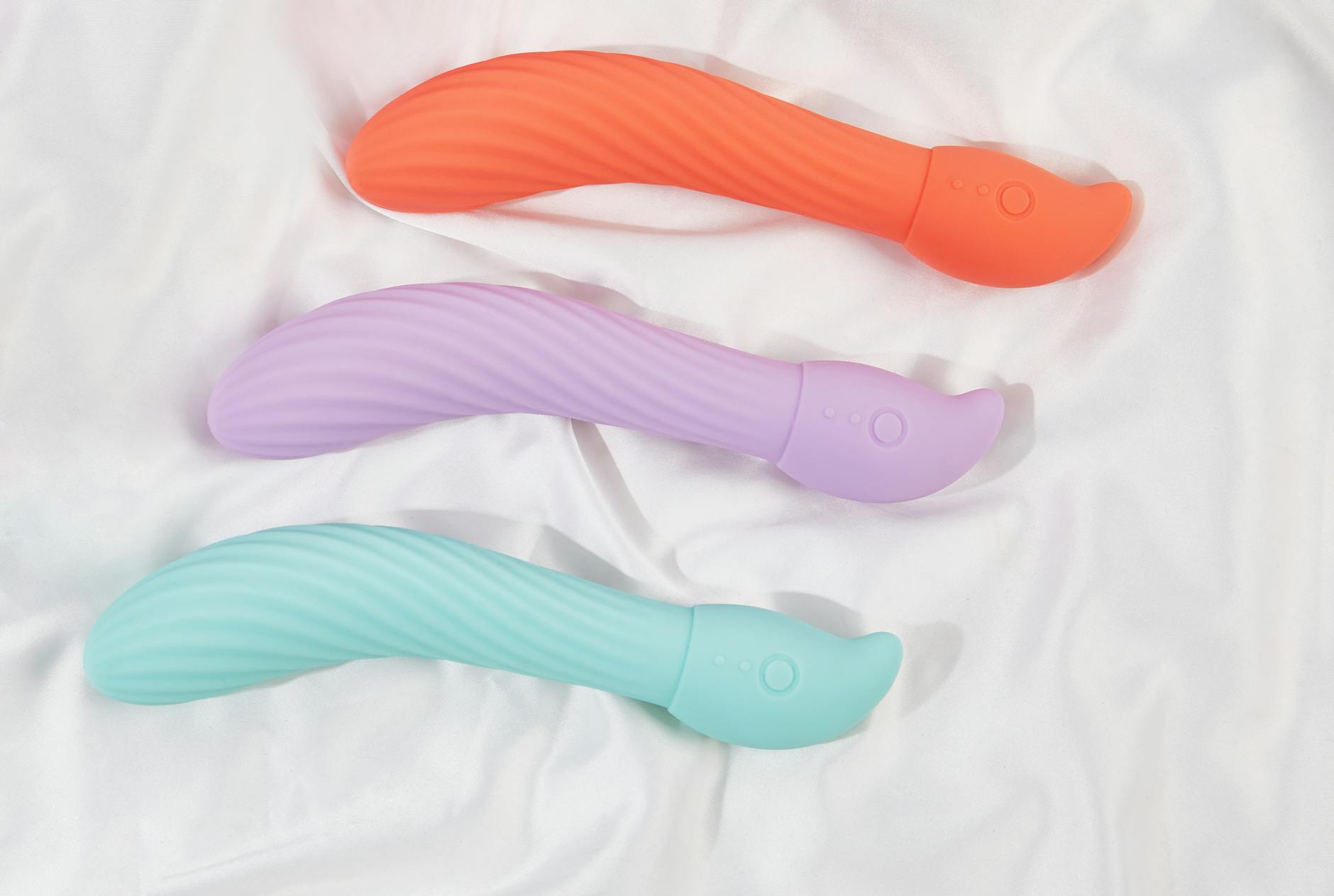 Three colorful clitoral vibrators arranged on white fabric, highlighting their smooth silicone design and texture.