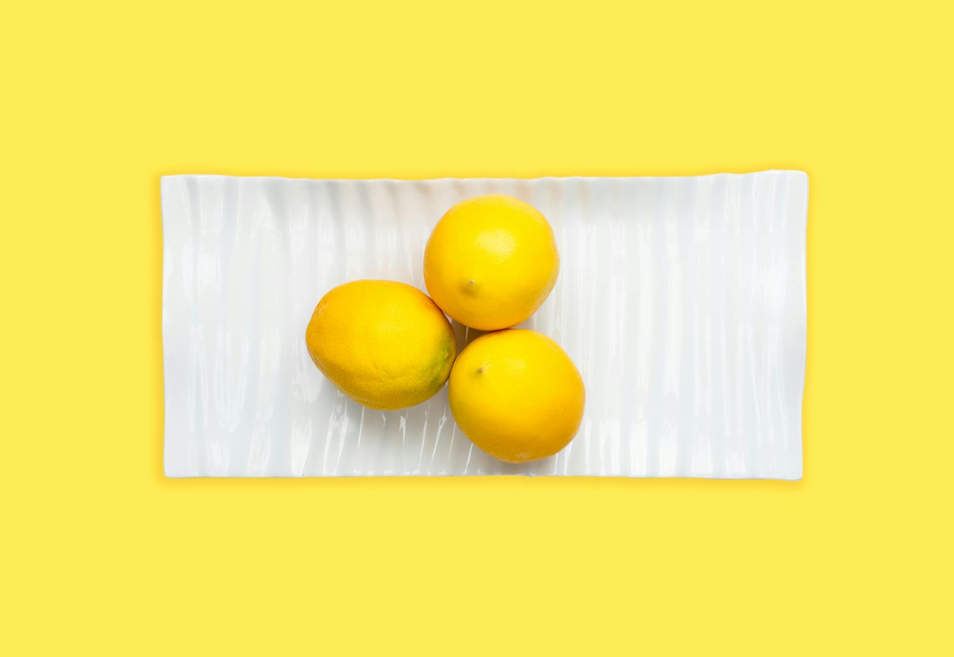 Fresh lemons on white plate against yellow background symbolizing renewal and freshness