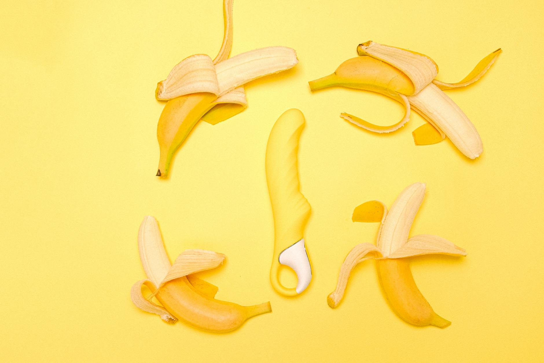 Yellow silicone clitoral vibrator surrounded by fresh bananas on a bright yellow background