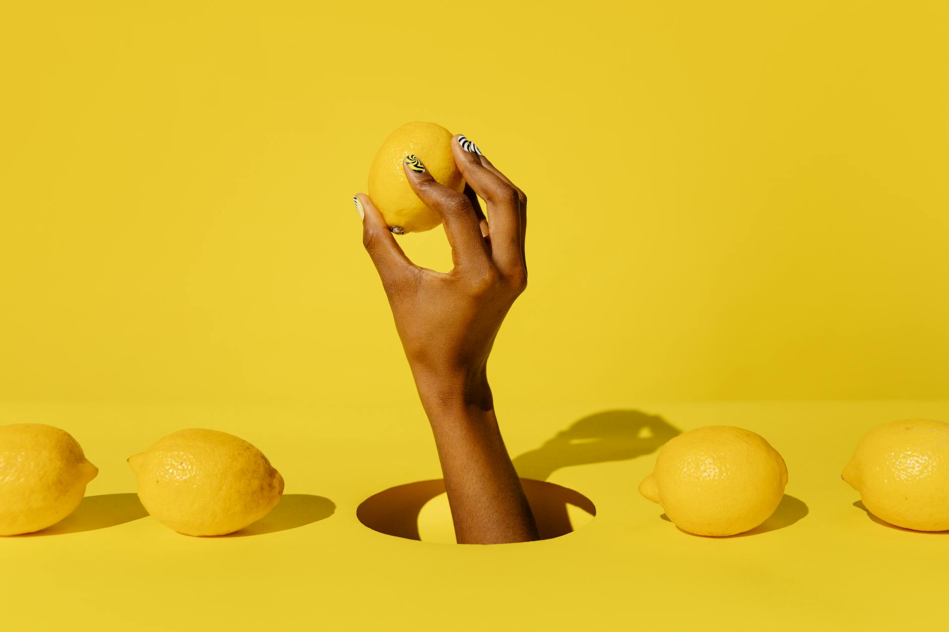 A hand holding a fresh lemon against a bright yellow background, symbolizing vibrant pleasure and wellness