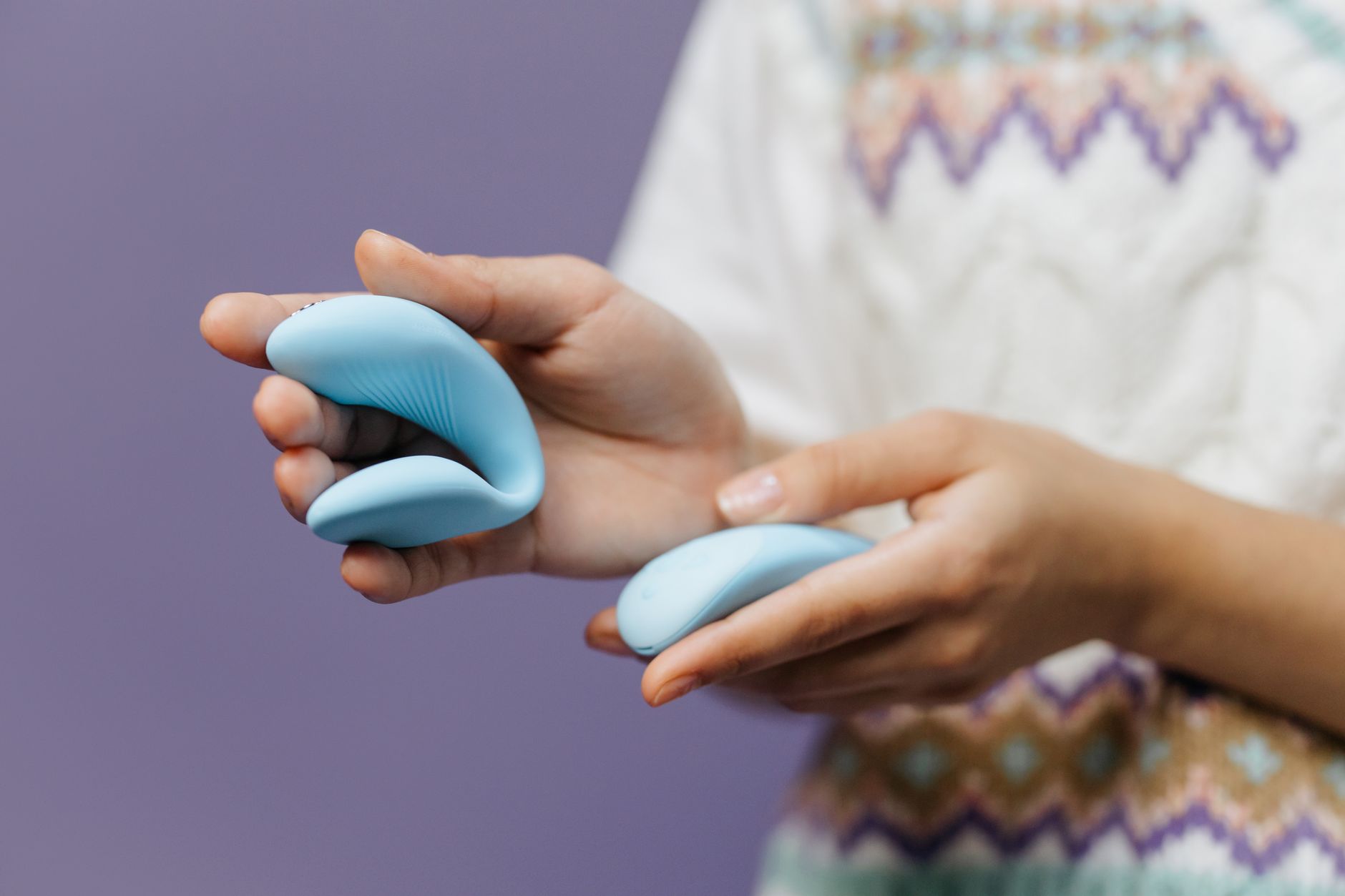 Close-up of hands holding a sleek lemon clitoral vibrator against a purple background.