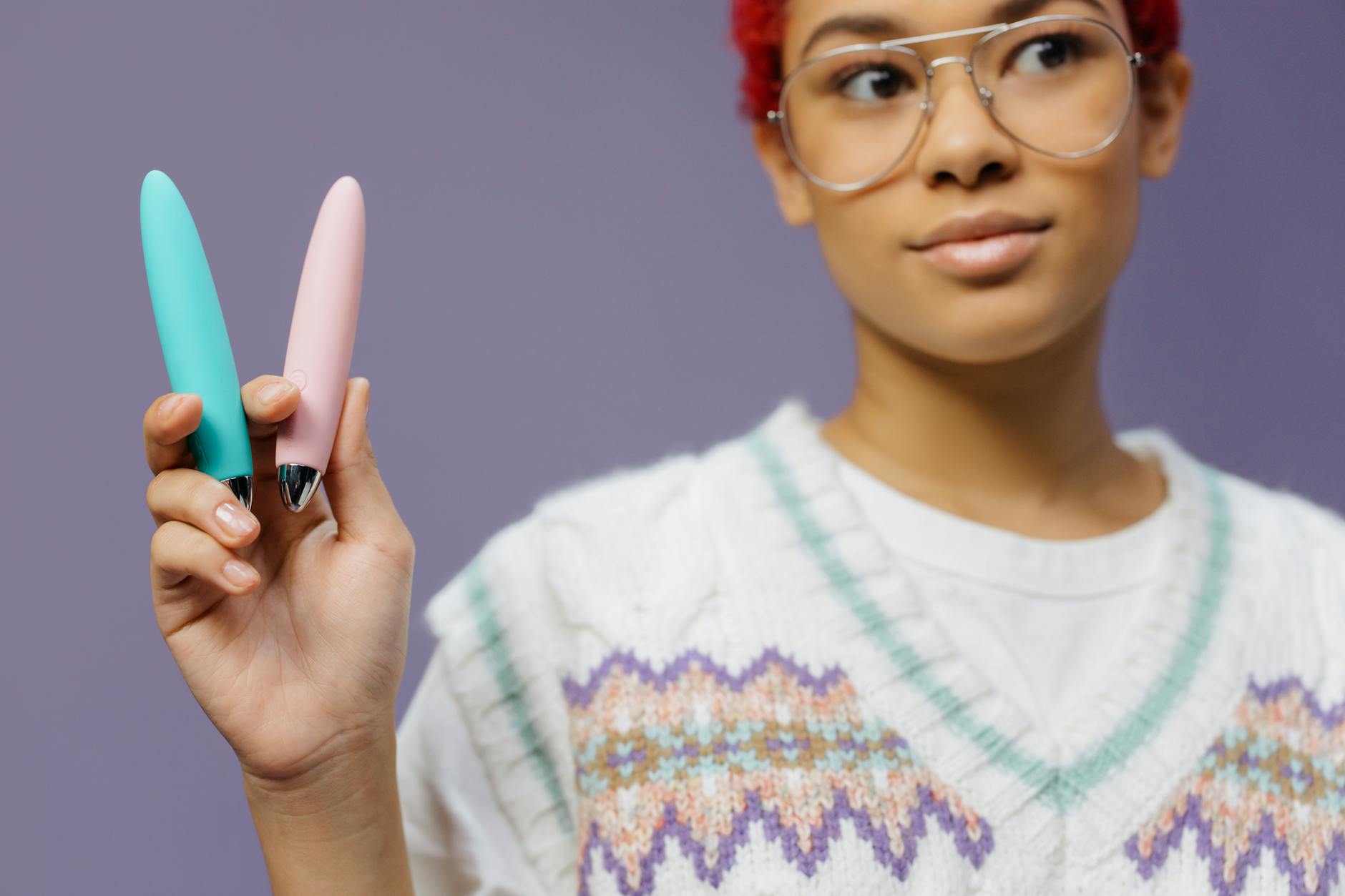 Woman holding colorful clitoral vibrators against a purple background, symbolizing reclaiming pleasure after breakup.