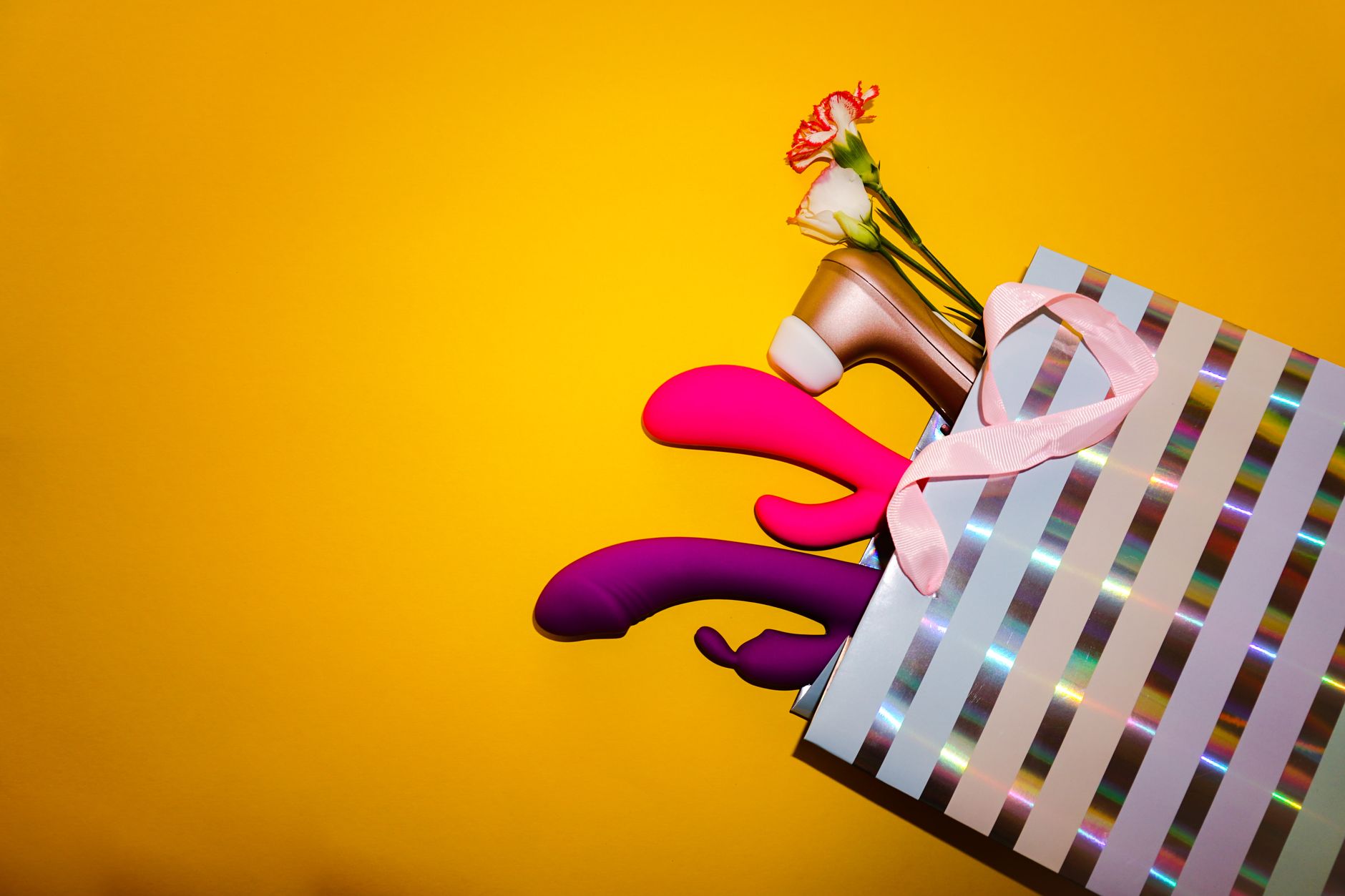Colorful vibrators with flowers in a holistic gift arrangement against a bright yellow background.