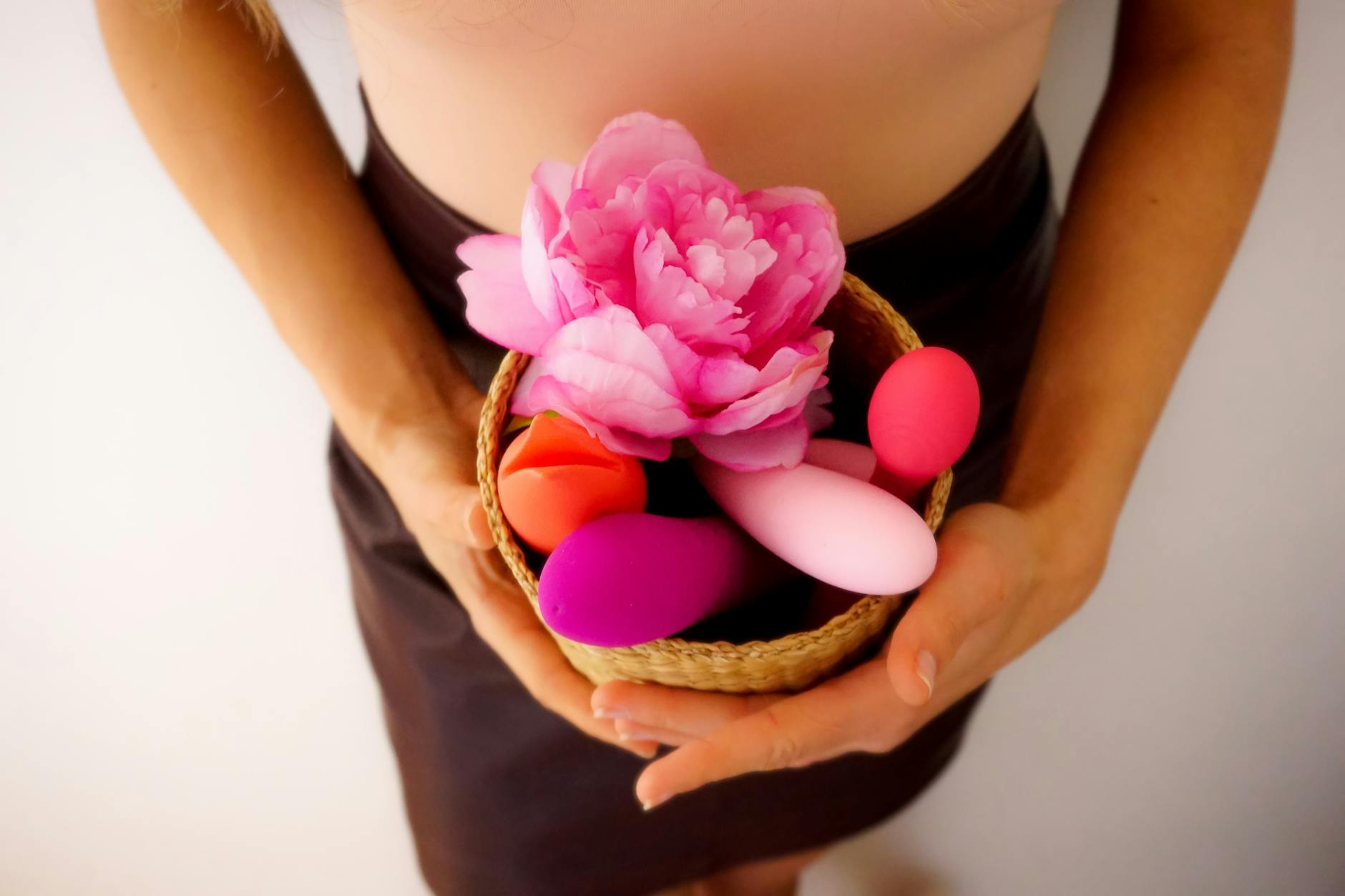 A hand holding a basket containing colorful vibrators and a pink flower.